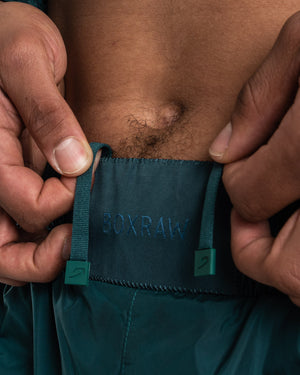 Man in a green sauna suit tracksuit with a white boxraw logo on the chest as well as adjustable wrist straps and made from polyester.